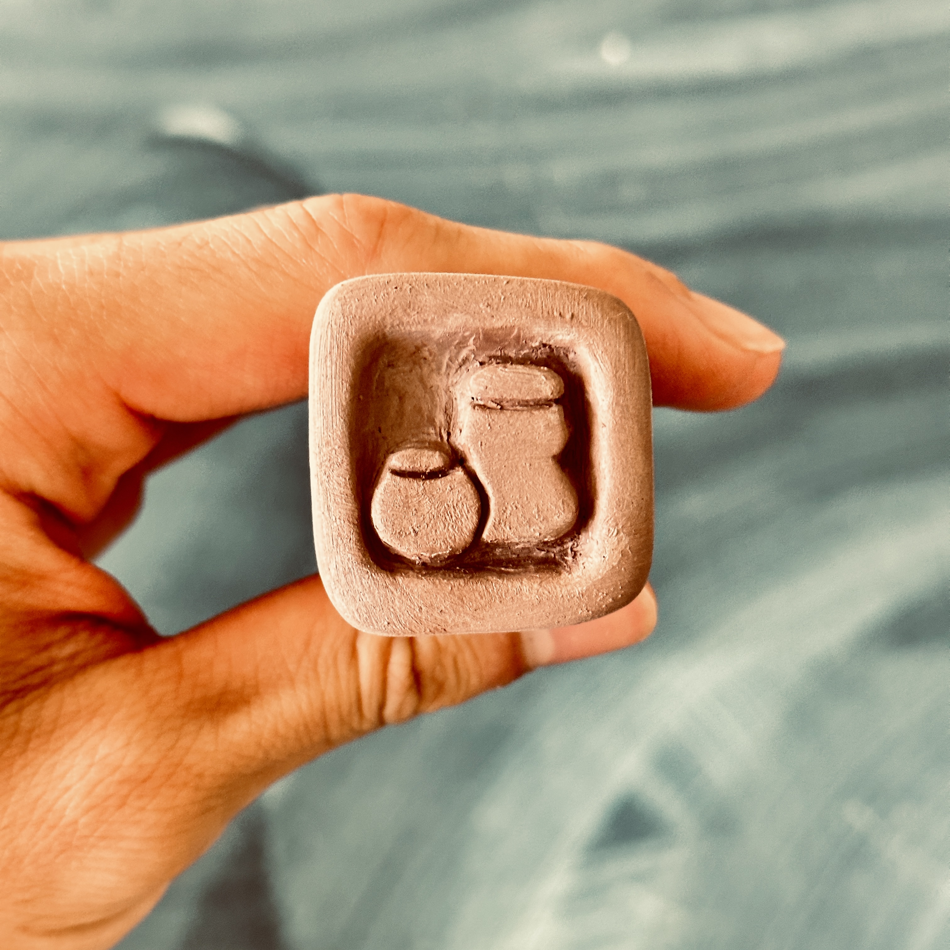 A bone dry terracotta stamp with a logo of two ceramic vessels carved into it.